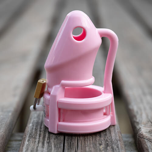 Pink HoD100 silicone chastity cage propped vertically on a wooden table.