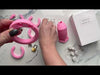 Assembling the pink HoD602 kit with all of the parts laid out on a marble top table. The video starts with the ring then attaches the cage before it's locked together with a brass padlock.